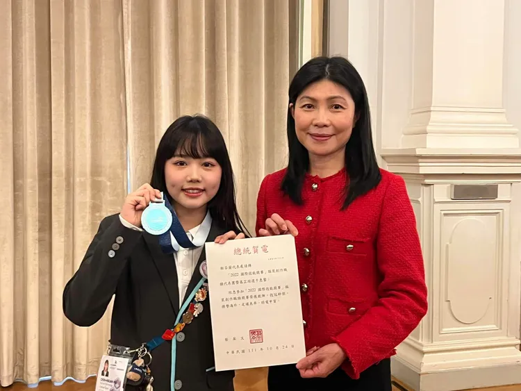 駐芬蘭代表張秀禎（右）代轉總統蔡英文、副總統賴清德給奪得服裝創作世界銀牌的慕芷瑄（左）賀電。教育局提供