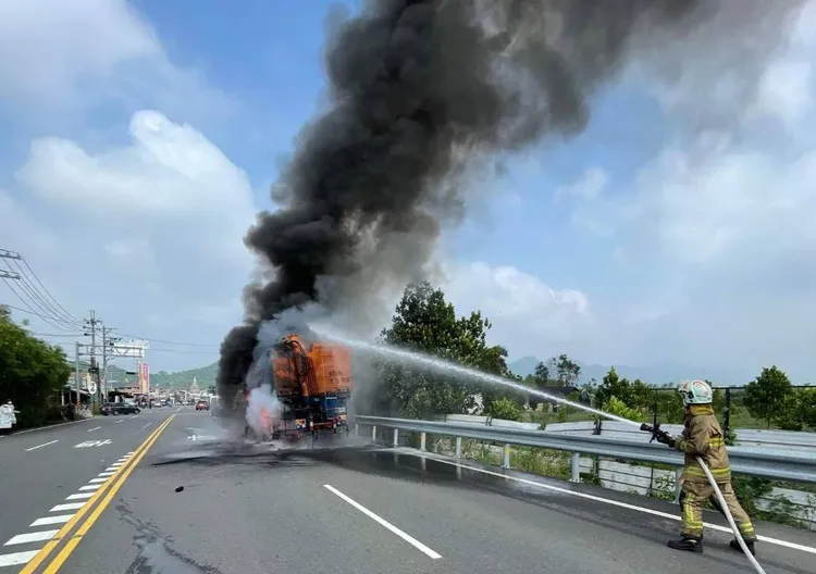 一輛載運飼料的大貨車左後輪突起火，消防人員射水滅火。讀者提供