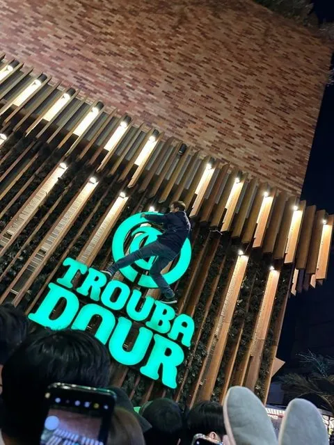 男子爬到當地店家招牌上，引來大批民眾注目拍照。翻攝自論壇PTT