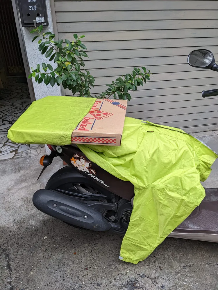 先用雨衣下擺將披薩盒包住，平放在機車後座上。翻攝自臉書/ Costco好市多 商品經驗老實說