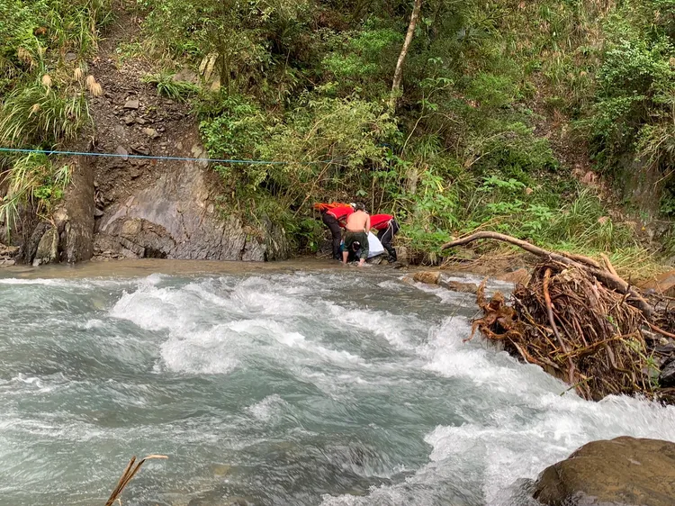 警消溯溪抵達河岸，發現該名婦人已死亡，以屍袋包裹後利用繩索搬運至安全處所。讀者提供