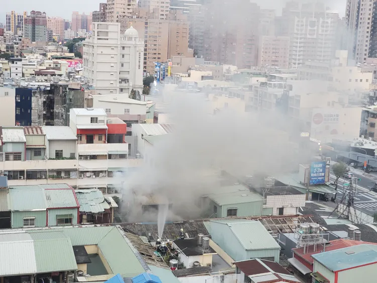 消防弟兄爬上另一排透天厝頂樓，朝起火點噴水滅火。王勇超攝