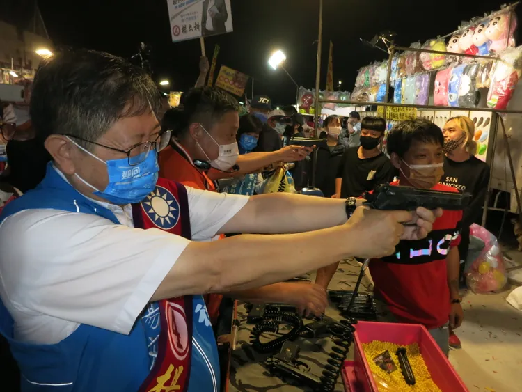 楊文科接受攤位老闆的邀請，體驗射氣球。楊文科競辦提供