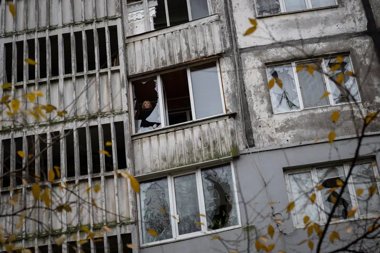 烏克蘭南部大城赫爾松（Kherson）一處因砲火毀損的住宅大樓裡，有住戶24日透過破裂的窗戶望向戶外。美聯社