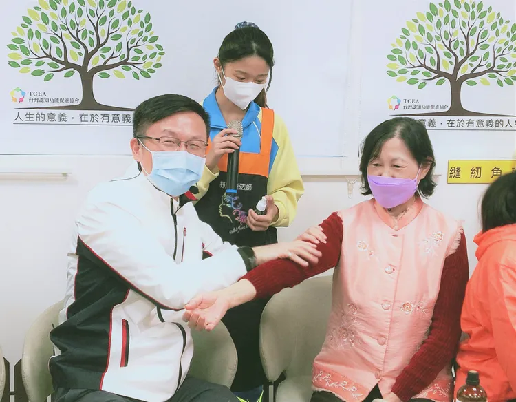 樹人家商美容科學生教導張明文局長(左)幫長輩按摩手部。新北市府提供