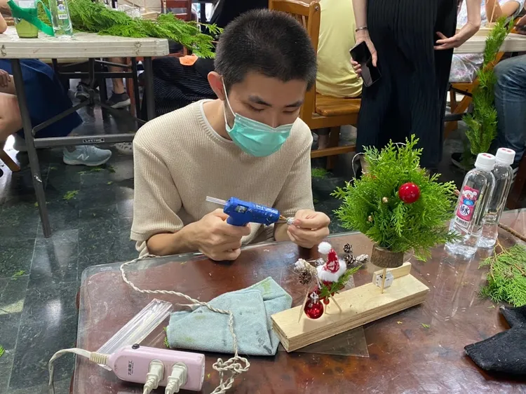 越南新二代阿順將松果以熱熔膠固定在聖誕樹底座，營造聖誕節氣氛。移民署提供