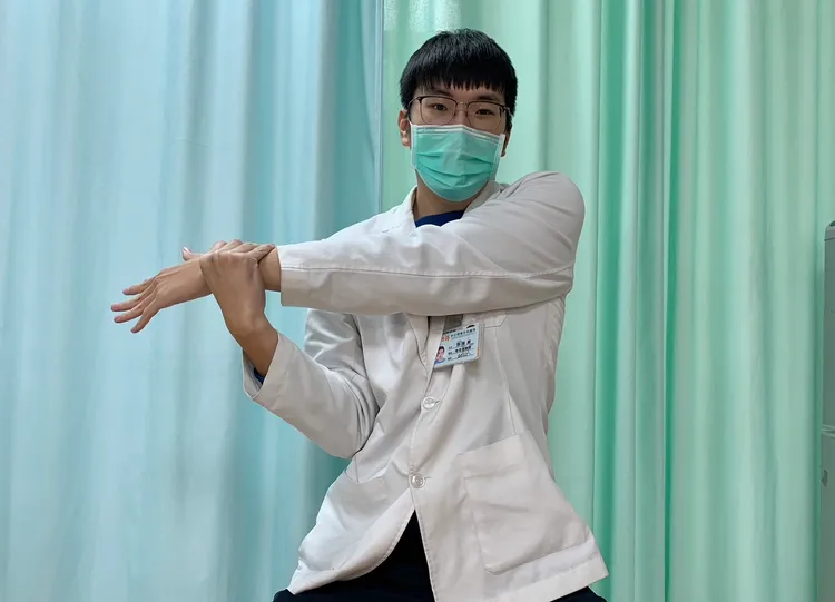 第一式「手臂交叉伸展」，坐著對側手抓伸展側手的腕部將手臂水平橫跨身體至對側伸展牽拉。讀者提供