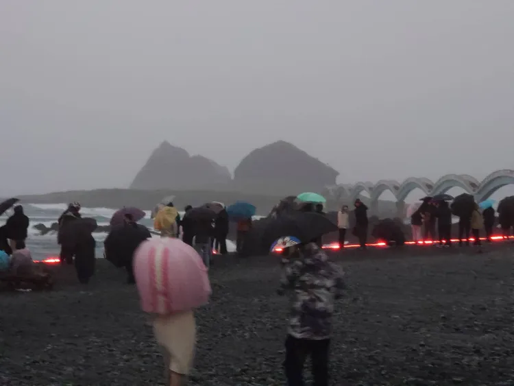 三仙台沙灘上遊客穿著雨衣撐傘等待曙光。翻攝畫面