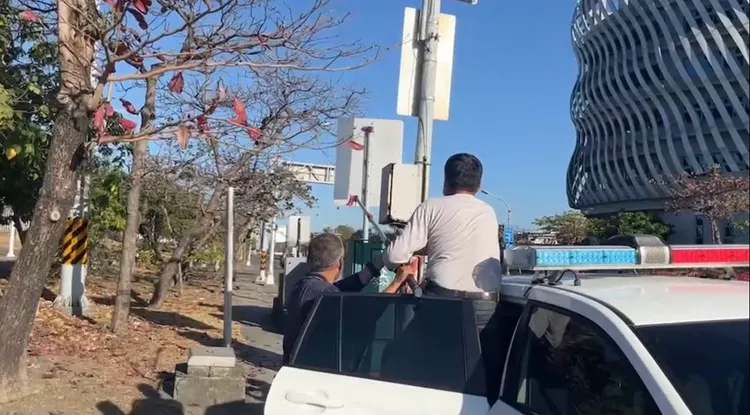 警方今到旗津風車公園旁，站在警車上，持工具移除纏繞在路樹上的風箏線。讀者提供