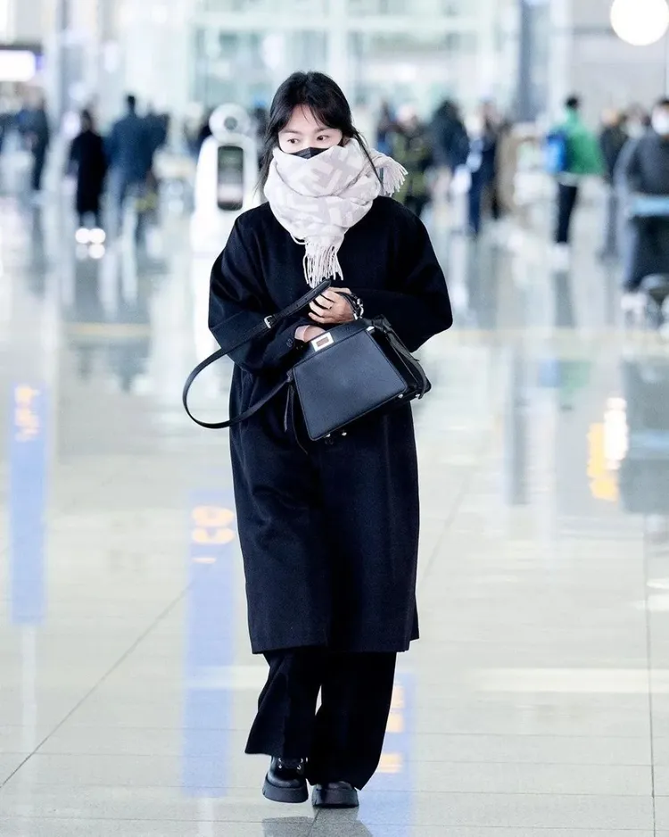 宋慧喬以黑色大衣、黑寬褲與黑鞋、黑色peekaboo手提肩背包的全黑裝扮，戴著口罩、FENDI字樣印花淺灰色圍巾遮半臉現身機場。翻攝dispatch_style IG