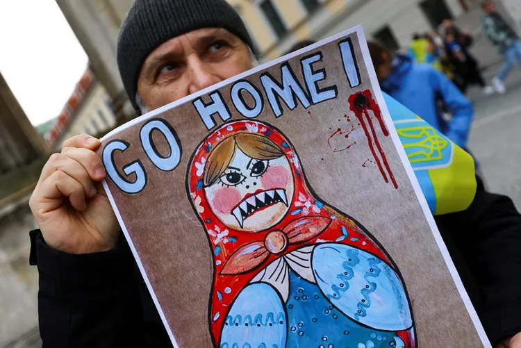 民眾手持俄羅斯娃娃圖像，上方寫「回家」。路透社