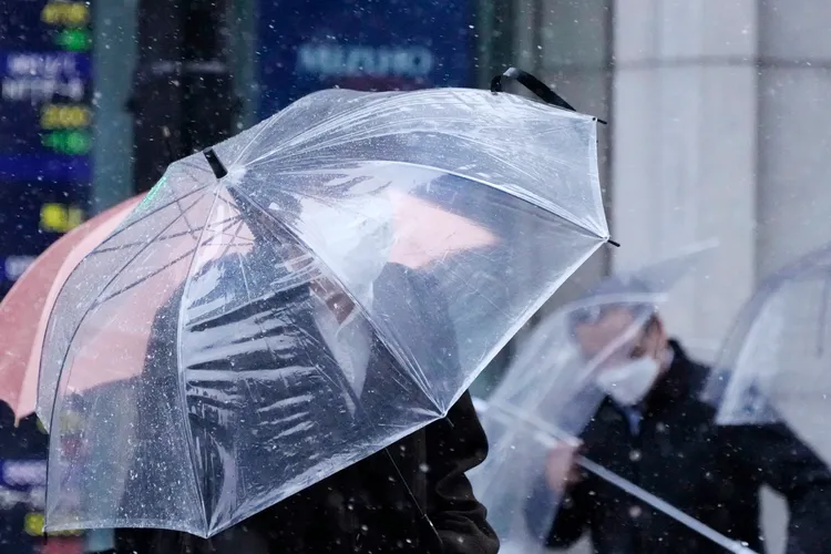 行人10日在東京街頭，被風雪吹到雨傘快撐不住。美聯社