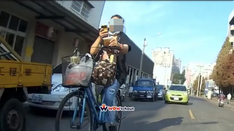 女單車騎士左手拎著飲料騎車，右手還拿手機盯著看。翻攝《WoWtchout-地圖型行車影像分享平台》YouTube頻道