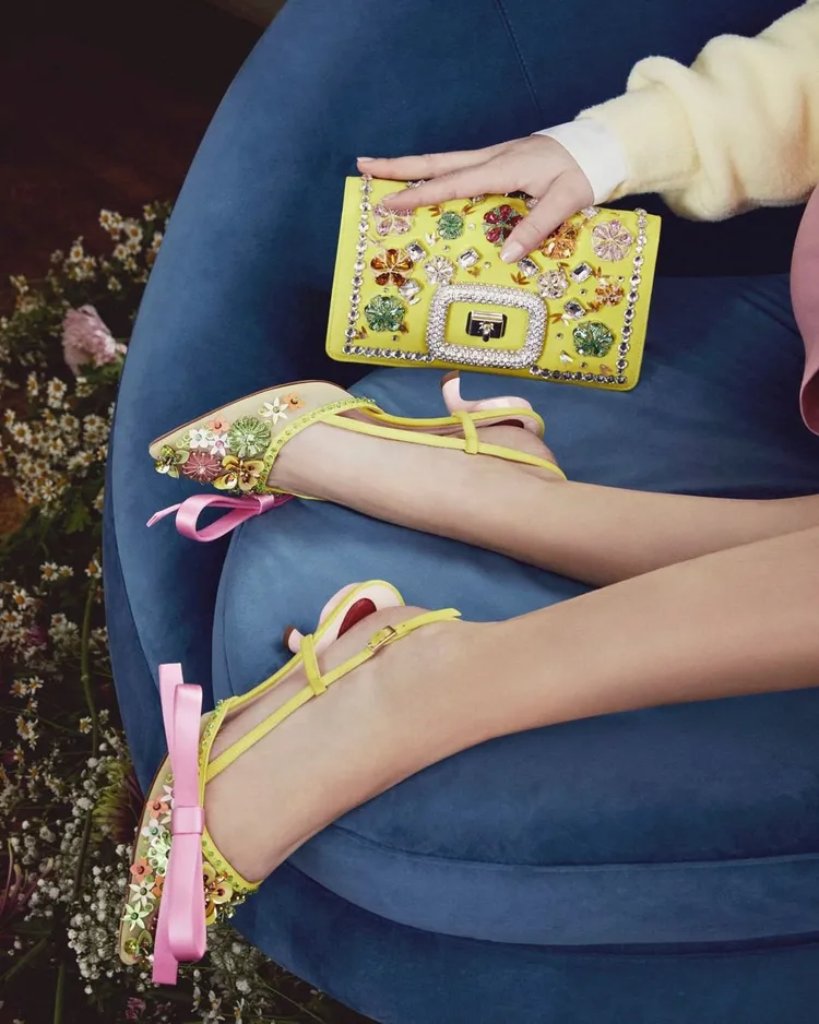 花團錦簇的豐饒意象，亦被轉譯為Virgule Flower Bow繫帶露踝尖頭鞋以及Viv’ Choc包款表面。品牌提供