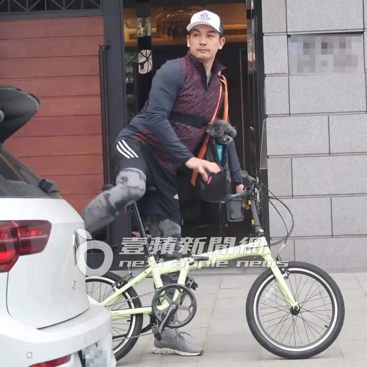 伊正頭載帽子，手提著寵物袋，一身運動勁裝騎腳踏車。特勤中心攝