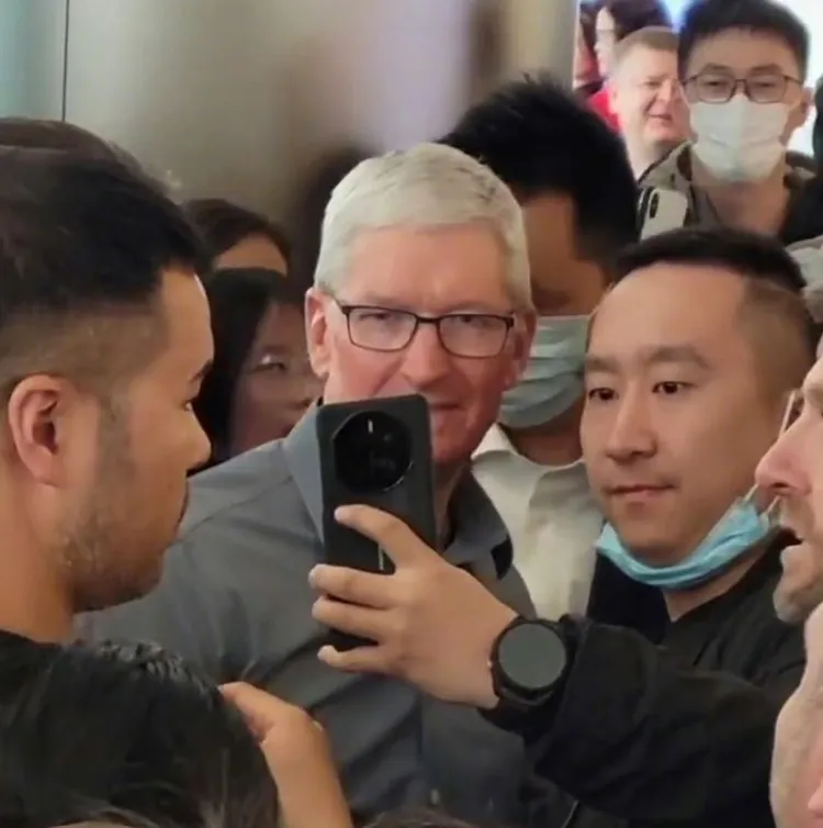 庫克昨參觀北京王府井Apple零售店，有人拿華為手機戴華為手表與他合照，庫克表情顯得非常僵硬。翻攝電商報