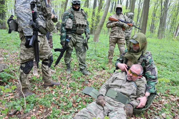 烏克蘭西部大城利維夫郊外森林27日有2組人馬分別進行傷兵撤離演習及無人機操作，這群人毫無軍事經驗，心裡惦記「保命第一、撐到醫護來」。圖為民防教官示範為傷兵頸部止血要領。中央社