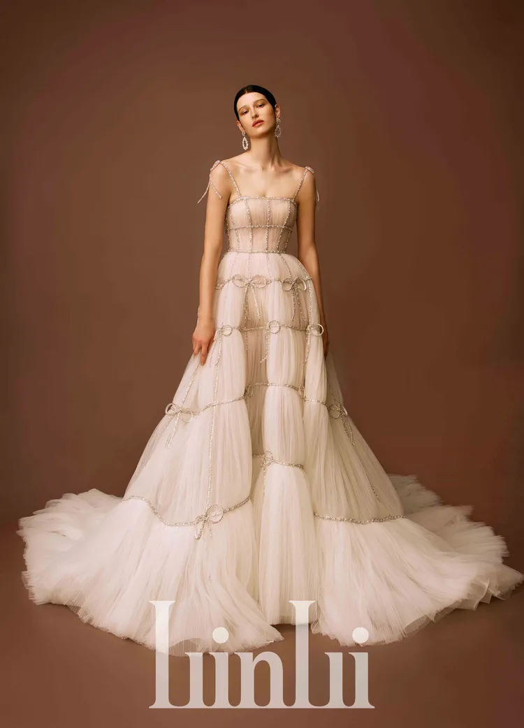 白標高訂系列手縫水鑽蝴蝶透視壓褶白紗，以輕型結構搭配重工鑽飾，透視鋪壓褶網紗上縫綴水晶珠條與蝴蝶結裝飾，穿上後像一個包裝精美的禮物。品牌提供