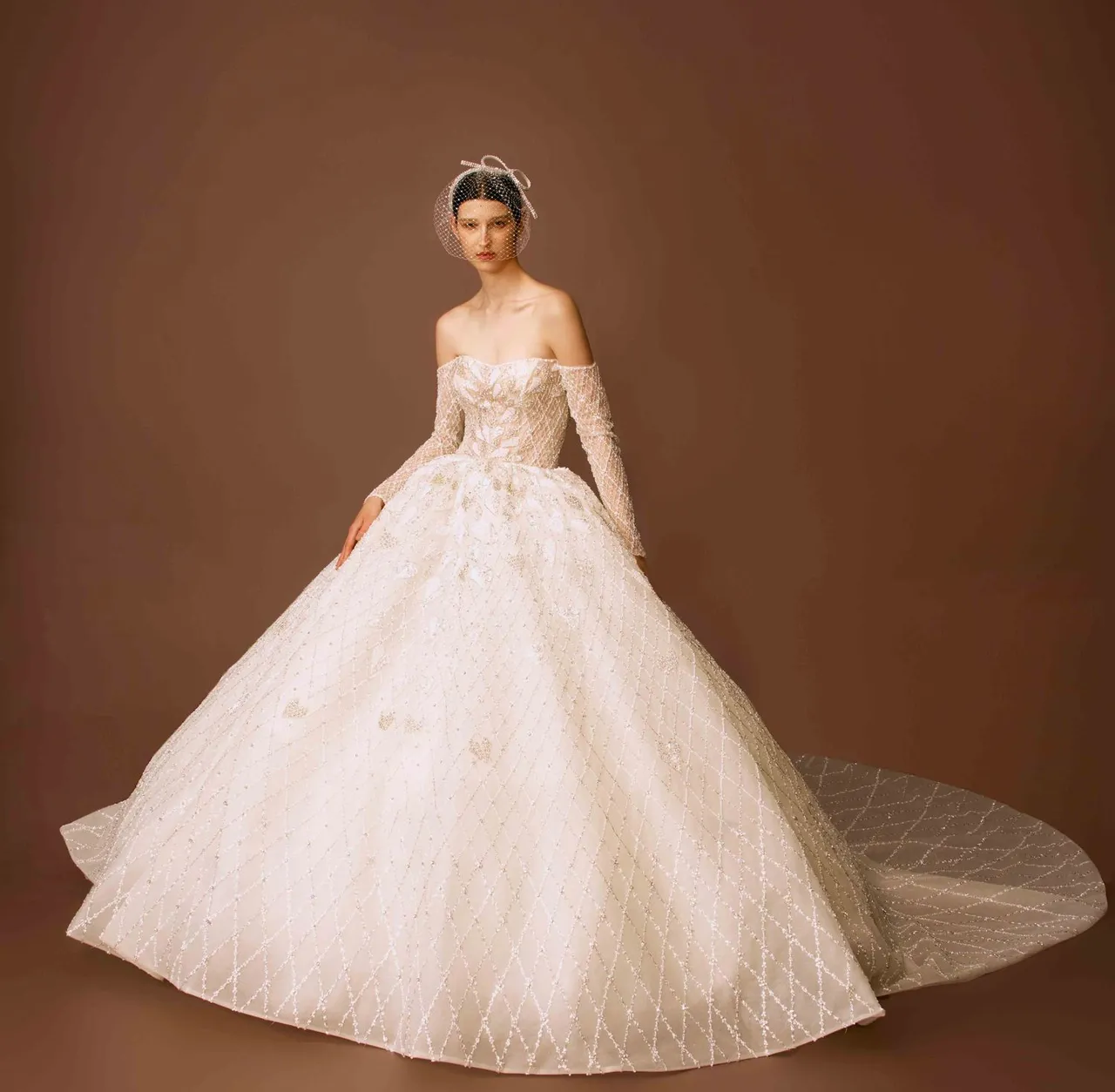 白标系列Kristal heart爱心菱格裸缝白纱，以落肩长袖的公主大蓬设计裙，上身运用几何爱心的排列，渐变到下身裙摆的菱格排列借以拉长比例，搭配复古感的发箍头纱是一大亮点。品牌提供