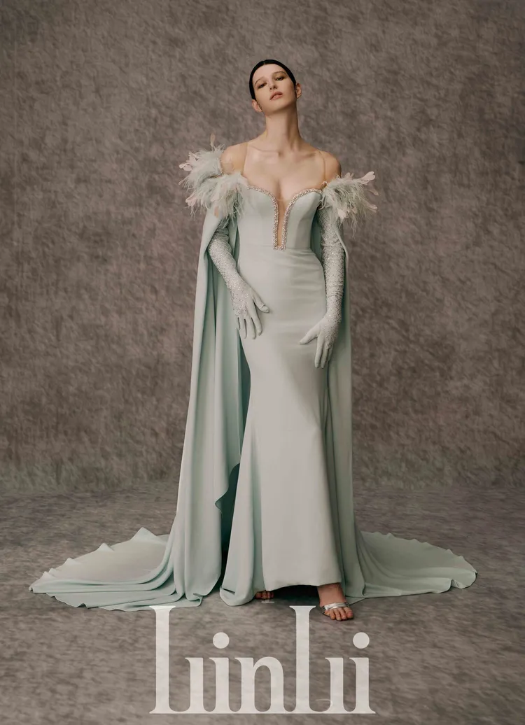 白標系列湖綠藍披風窄擺禮服，以 合臀窄襬剪裁勾勒身體曲線，更顯成熟韻味，運用時裝禮服常用的霧面緞布染成獨特湖綠藍，做出整體披風式禮服，搭配同素材水晶燙飾手套，風格華麗高貴。品牌提供