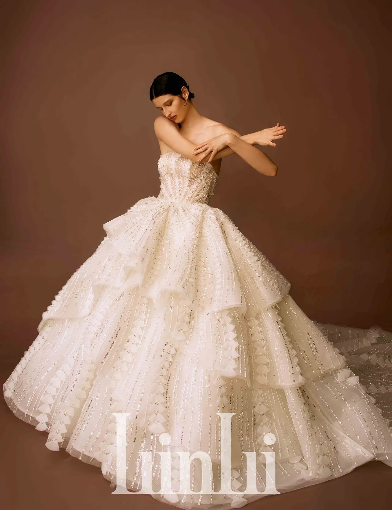 黑标顶级高订系列的手工三角型裸缝立体白纱，以手工将乌干纱压制出不同大小圆形花片，再一一折成三角形状地堆叠排列出流线线条于白纱上，并缝缀施华洛世奇水晶裸珠条，为蛋糕荷叶裙创造出层次流动的梦幻气息。品牌提供