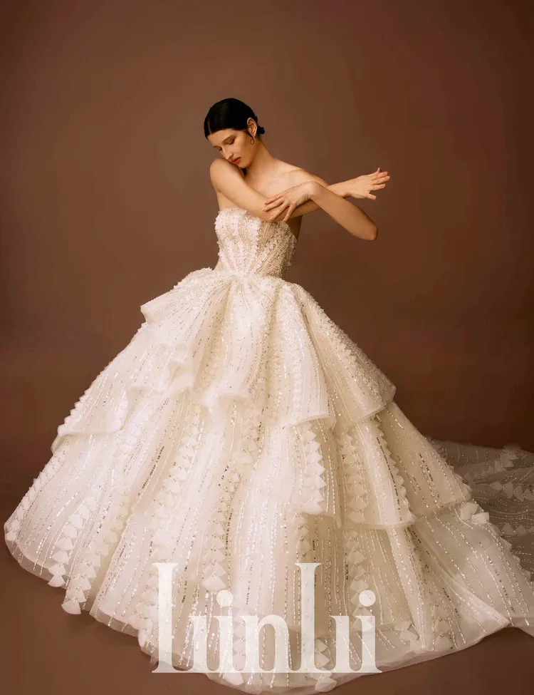 黑標頂級高訂系列的手工三角型裸縫立體白紗，以手工將烏干紗壓製出不同大小圓形花片，再一一折成三角形狀地堆疊排列出流線線條於白紗上，並縫綴施華洛世奇水晶裸珠條，為蛋糕荷葉裙創造出層次流動的夢幻氣息。品牌提供