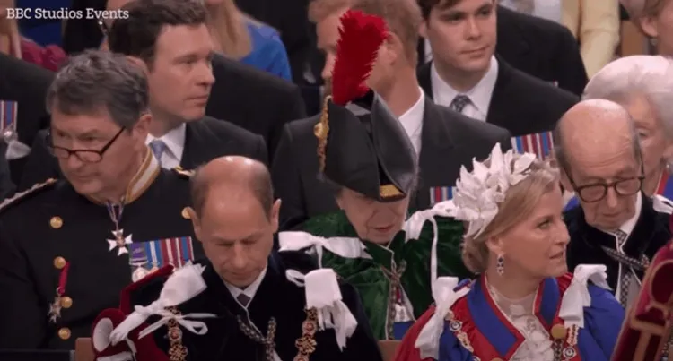 哈利王子的臉（中、鳥羽後方）被前排的姑姑安妮公主頭上那根巨大的鳥羽遮住了。翻攝BBC