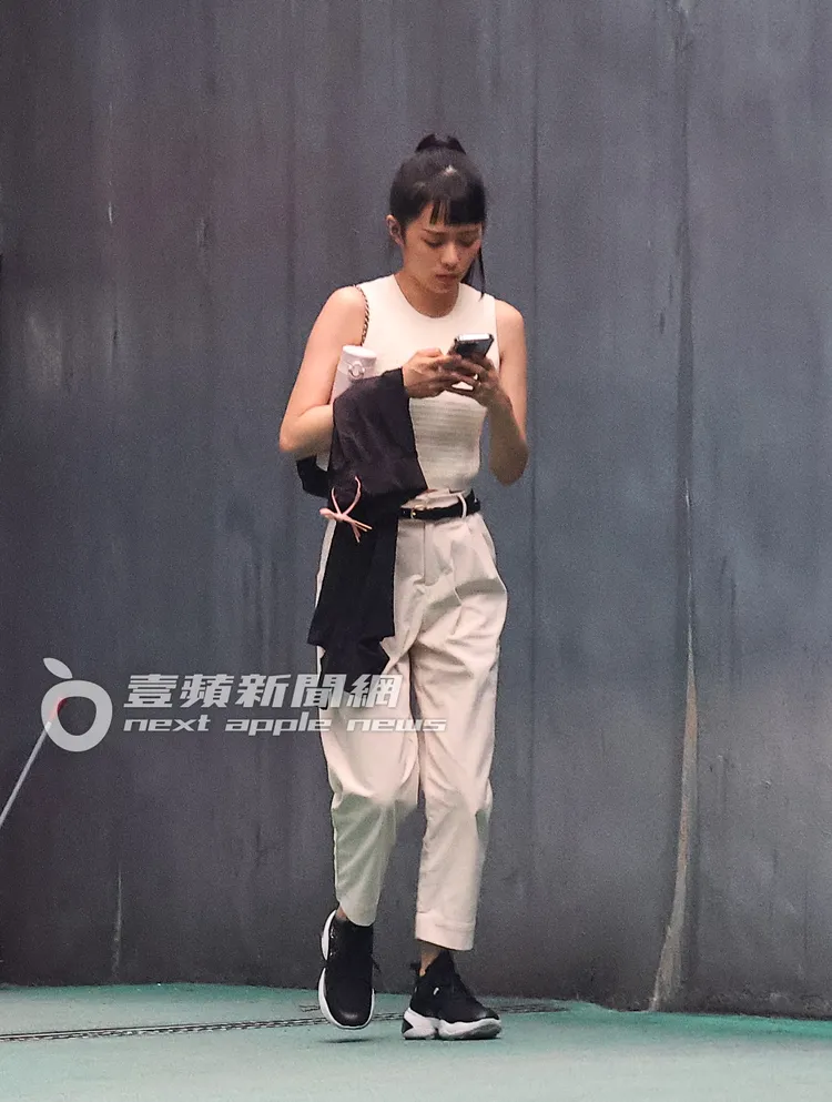 停妥車的簡廷芮，手臂掛著運動褲，一邊滑手機邊走出停車場。特勤中心攝