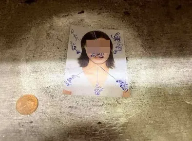 骨灰罈下壓著陌生女子的照片，並依不同方位書寫疑似泰國經文，此外還有錢幣。翻攝馬來西亞《中國報》