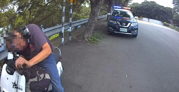 余男熱趴在機車上，引起巡邏警員注意，上前關切。民眾提供