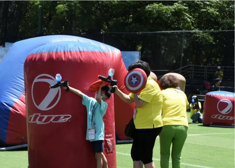 永達志工在烈日下不減熱情，陪伴弱勢孩童勇闖漆彈場。業者提供