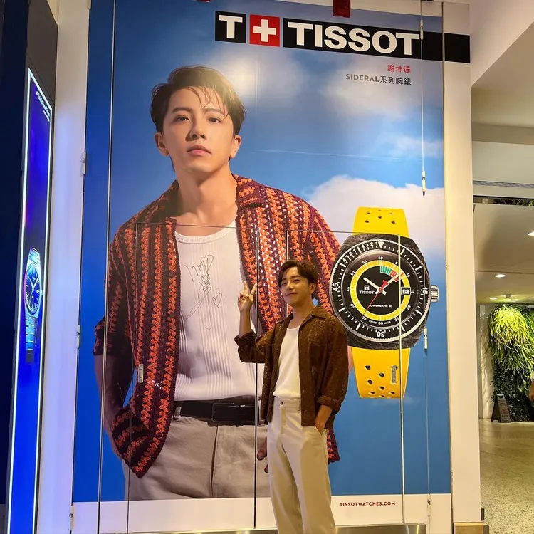 坤達開心與在天梭台北101專賣店外自己的巨型看板合影，還特地在上面簽名。翻攝hsieh_kunda IG