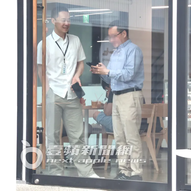 張承中（左）與友人站在咖啡廳櫥窗前相談甚歡。特勤中心攝