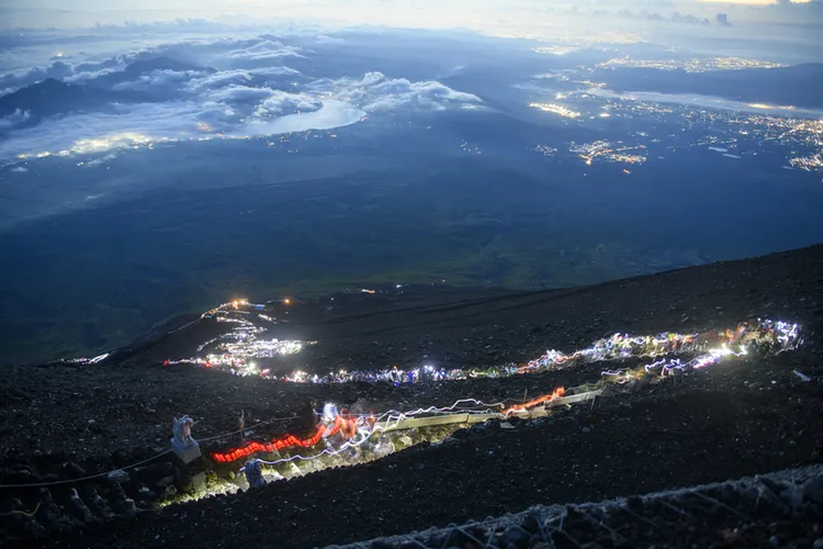 大批登山客夜間攀登富士山，趕在日出前攻頂，攜帶的照明設備形成一條發光的人龍。（山梨縣政府提供）中央社
