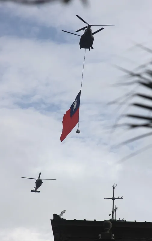 國軍28日展開空中全兵力預演，懸掛巨幅國旗的CH- 47SD運輸直升機飛越總統府前上空。 中央社
