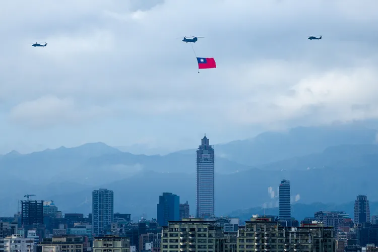 國軍28日展開空中全兵力預演，一架CH- 47SD契努克運輸直升機（中）吊掛國旗飛越台北市上 空。 中央社