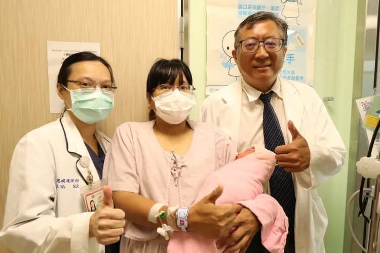 陳姓孕婦抱著在丈夫車內誕生的女兒，與亞大附醫產科主任陳泰昌及護理人員合照。院方提供