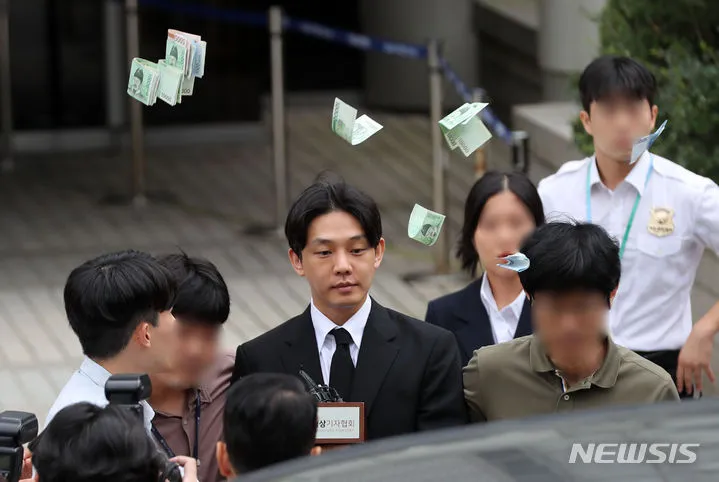 劉亞仁步出法院時，遭路人丟擲大把鈔票，送他當「保管金」，過程非常難堪。翻攝NEWSIS