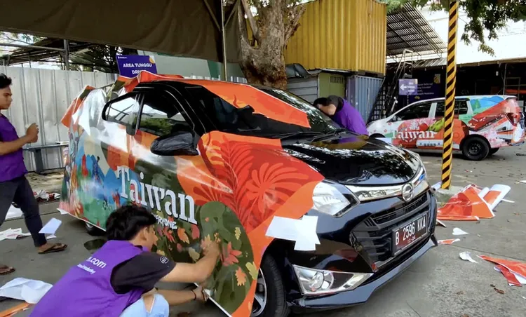 印尼工作人員將「KROOSYL」團隊設計的塗鴉黏貼在觀光汽車上。中央社/
 StickEarn提供