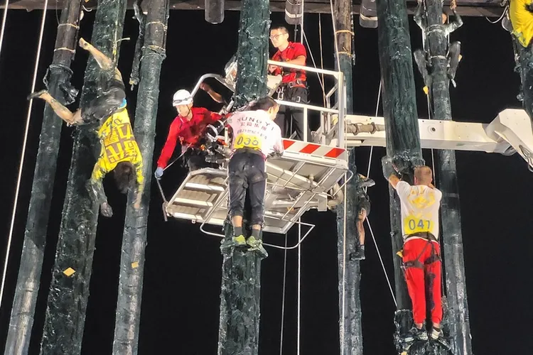 宜蘭頭城搶孤民俗活動14日深夜於當地舉辦，有參賽選手（左）疑因體力不支，在攀爬時墜落，所幸身上扣好安全扣，一度吊掛半空中，最後獲救。中央社