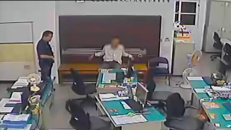 黃男雙手被銬，竟伸腳勾拉、踹踢辦公桌。警方提供