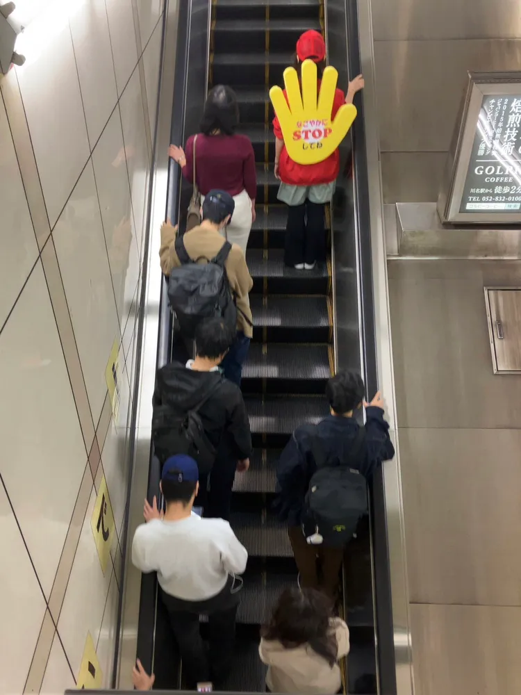 女員工背鮮黃色顯眼的半身高手掌形狀告示牌勸阻旅客行走，翻攝自推特「じゅん@Rabbit_D06」