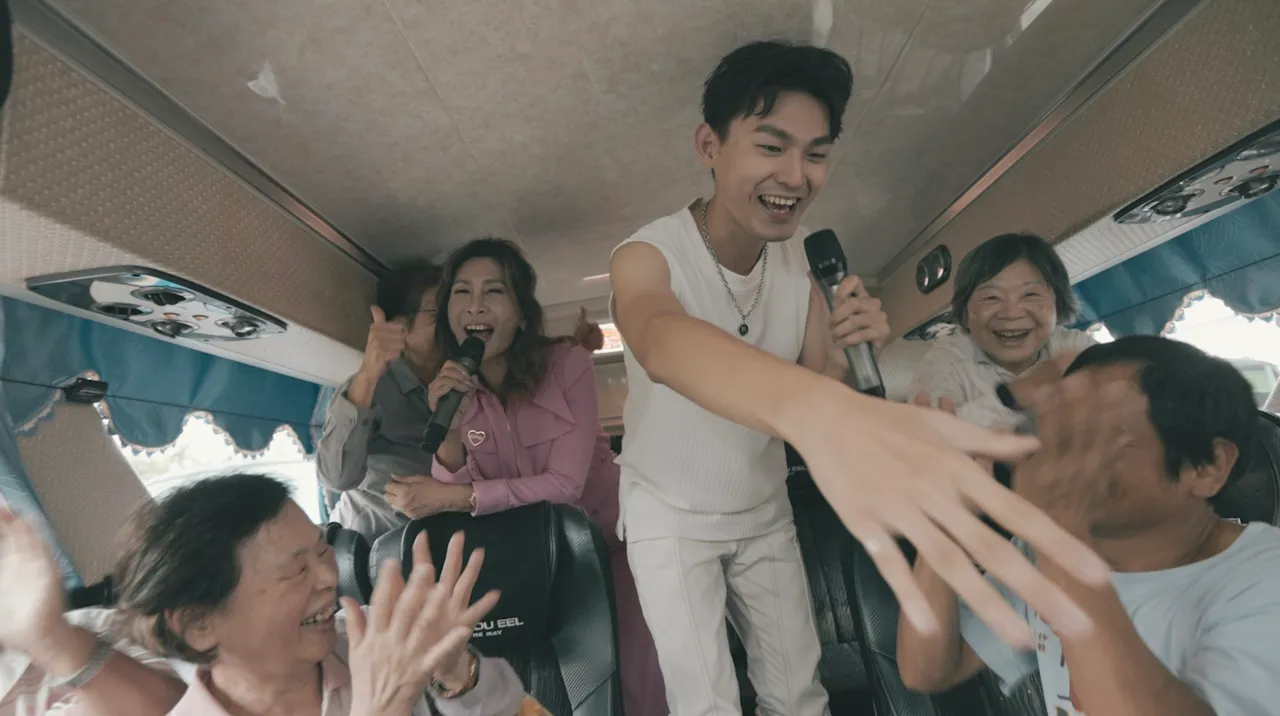 羅梓華（右）與陳燕萍遊覽車上合拍MV，受到阿公阿嬤空前歡迎。威爾斯葛羅提供