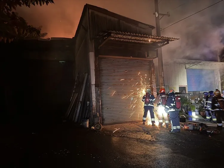 新北市蘆洲區1處連棟鐵皮工廠27日晚間發生火警，消防員破壞鐵門入內灌救。 （翻攝照片） 中央社