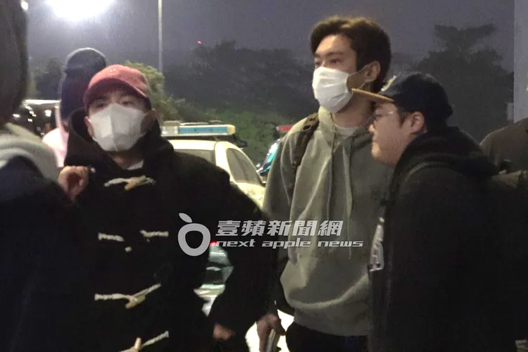 SJ厲旭（左）戴紅色鴨舌帽，穿黑色大衣，跟始源站在機場出境大廳外等候。特勤中心攝