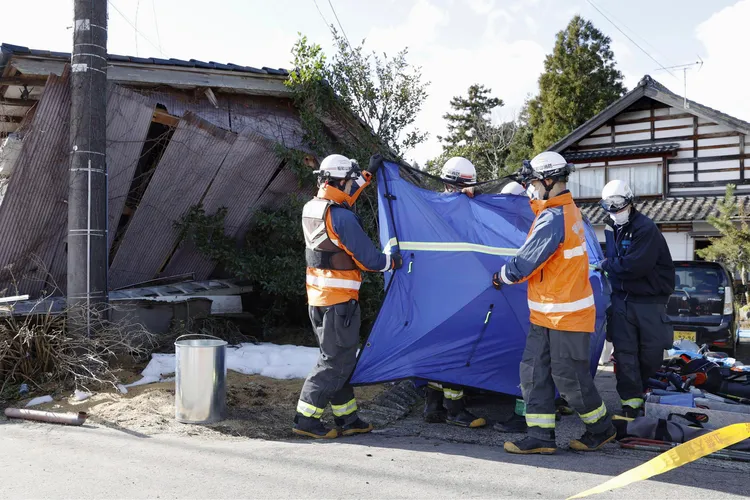 救難人員在珠洲市從瓦礫堆下找出遺體，在藍布遮掩下送出廢墟。美聯社