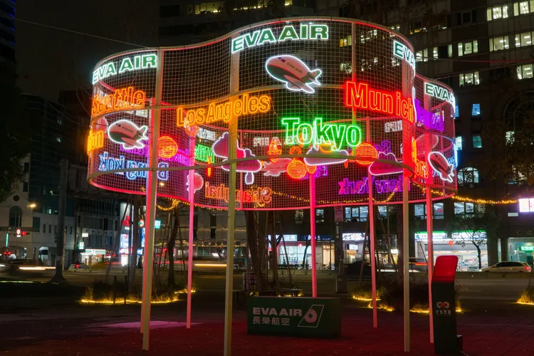 長榮航空「翱翔雲端」以白色金屬雲朵意象結合熱門航點燈飾文字，讓民眾與Q版飛機一起環遊世界。北市觀傳局提供