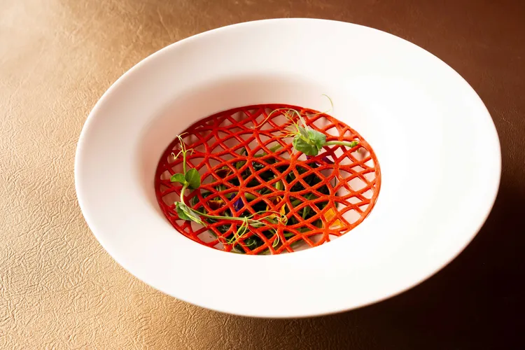 《AW Restaurant秋・現代法餐》套餐結合春節傳統元素，以招財銅幣為意象設計餅片，與下面的芥藍菜搭配增加口感，視覺感十足。業者提供