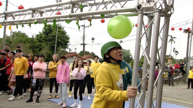 阿龐玩遊戲，拼命要用把安全帽砸破頭頂上的氣球。民視提供