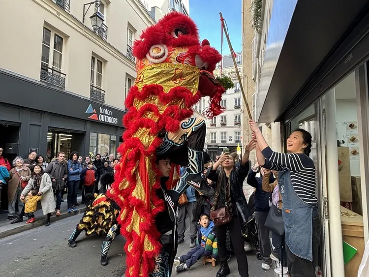 17日巴黎市台灣車輪餅店Ciao Roue前門庭若市。法國人古思萬帶領的「法國民社館忠義堂」正在表演舞獅的「採青」橋段，採青如今衍生之意取生菜和「生財」的諧音，為商家帶來好彩頭。中央社
